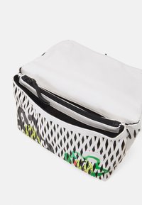 Hvid struktureret taske med lynlås og et diamantmønstret design. Den har farverige detaljer og et elegant sort interiør.