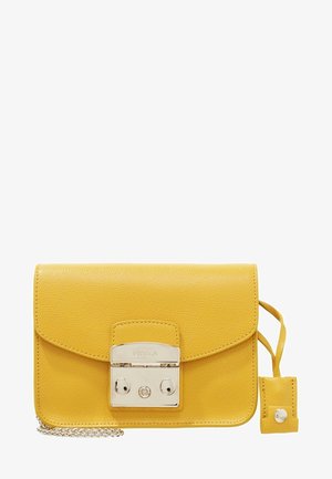 Sac bandoulière en cuir jaune avec fermoir argenté, bandoulière chaîne, et plaque métallique de marque sur le rabat avant.