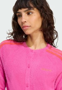 Fuzzy pink cardigan with a round neckline, five buttons, and orange accent stripes on the shoulders. Features a subtle logo on the chest.