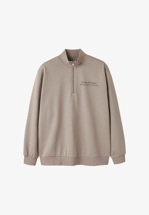 Beež pool lukuga pusa pikkade varrukatega, soonikkoes mansettidega ja tekstiga "Porte d'Auteuil" koos koordinaatidega vasakul rinnal.