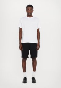 Tricou alb cu manșete scurte și detalii roz la guler, asortat cu pantaloni scurți negri. Mocasini negri și șosete albe cu dungi finalizează ținuta.