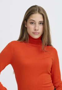 Piros garbó pulóver sima, rugalmas anyagból készült. Hosszú ujjaival és testhezálló dizájnjával egy világos háttér előtt látható.