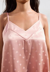 Pink satin camisole featuring a V-neckline, thin straps, and a heart pattern on the fabric, smooth texture with a loose fit.
