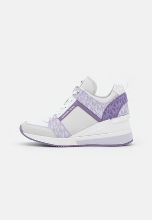 Sneaker Michael Kors bianca e viola con tacco a zeppa, pannelli laterali decorati e lacci bianchi, mostrata di lato su sfondo grigio.