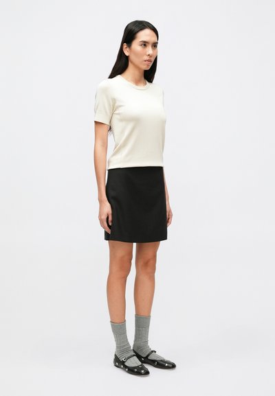 Īsroku krēmkrāsas tops kopā ar melnu svārku. Valkāts ar pelēkām ribotām zeķēm un melnām kurpēm ar dekoratīviem metāla akcentiem.