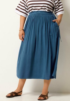 Person iført en blå gathered midi-nederdel med bundet talje, stribet kortærmet top, brune sandaler og et armbånd på det ene håndled.