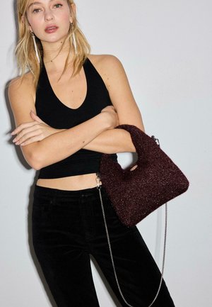 Weinroter glitzernder Handtasche mit strukturierter Oberfläche, ausgestattet mit einem kurzen Henkel und einem langen silbernen Kettenriemen. Getragen zu einem schwarzen Outfit.