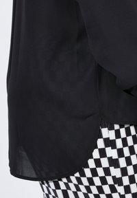 Schwarzes transparentes Oberteil mit abgerundetem Saum, kombiniert mit einem schwarz-weißen karierte Muster am unteren Teil, das einen strukturierten Stoff zeigt.