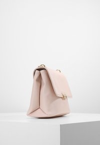 Světle růžová kabelka s pevnou konstrukcí, která má texturovaný povrch, zlaté kovové zapínání a klopový uzávěr.