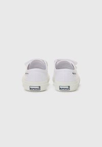 Zapatillas de lona blancas con punta redonda, suela de goma plana y cierre de cordones, con un logo en el talón y en la lengua.