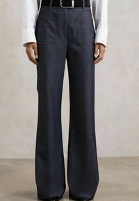 Pantaloni evazați din țesătură de un albastru închis, cu o textură netedă, două buzunare frontale și un brâu subțire cu o cataramă strălucitoare.