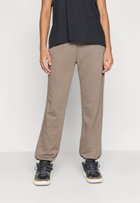 Lettebukser i lysebrun, lavet af blødt stof. De har en løs pasform, elastisk talje, og er parret med sorte sportssko.