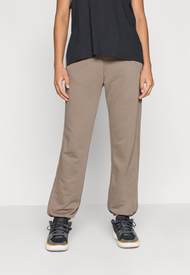 Lettebukser i lysebrun, lavet af blødt stof. De har en løs pasform, elastisk talje, og er parret med sorte sportssko.