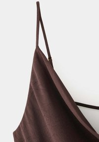 Gros plan d'un top marron foncé à fines bretelles en tissu légèrement texturé avec bretelle d'épaule ajustable, sur un fond clair uni.