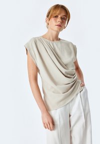 Beige draperen top met kapmouwen, vervaardigd van een zachte, gestructureerde stof en een relaxte pasvorm, gecombineerd met crèmekleurige wijde broekspijpen.