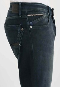 Jeans en denim foncé au design ajusté, avec un style classique à cinq poches, des coutures contrastantes et une patte en cuir à l'arrière.