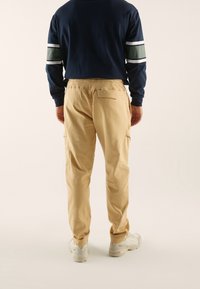 Granatowa bluza z kapturem z białymi i zielonymi paskami, zestawiona z jasnobeżowymi spodniami typu cargo z tylną kieszenią i elastycznym pasem, noszona z białymi trampkami.