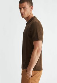 Polo shirt marrone a maniche corte con un design a maglia texture, caratterizzato da un colletto e polsini a coste, abbinato a pantaloni beige.