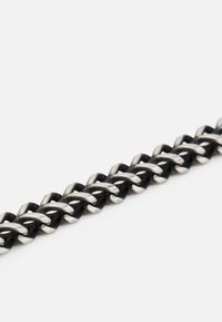 Bracelet en chaîne métallique avec des maillons noirs et argentés alternés, finition lisse et design tissé.