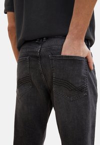 Jeans in denim nero con vestibilità dritta, dotati di due tasche posteriori con cuciture dettagliate e una finitura testurizzata.