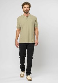 Khaki-paita, jossa on huomaamaton logo, lyhyet hihat ja klassinen kaulus, yhdistettynä mustiin housuihin ja vaaleanbeigeihin tennareihin. Sujuva rakenne.