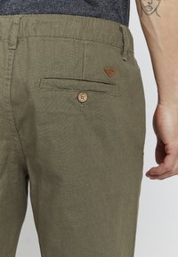 Khaki broek van een textuurstof met een achterzak, houten knoopsluiting en een klein leren logo label. Standaard pasvorm en ontwerp.