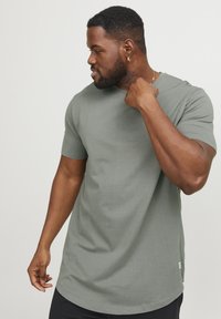 Short-sleeve, olive green t-shirt made of cotton. Features a crew neck and a straight hem, with a small branding tag at the lower side.