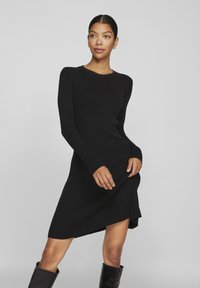 Μαύρο ριγέ φόρεμα με μακριά μανίκια, στρογγυλή λαιμόκοψη και ασύμμετρο στρίφωμα. Φτιαγμένο από υφασμάτινη πλέξη, με σφιχτή εφαρμογή.