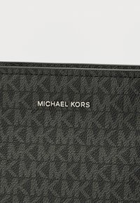 Carteira em tecido preto com textura, apresenta um logótipo gravado em prateado metálico, com um padrão de letras interligadas por toda a superfície.