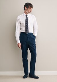 Camicia bianca, pantaloni blu navy a righe sottili, cravatta blu navy a pois e scarpe nere, con design classico e taglio su misura.