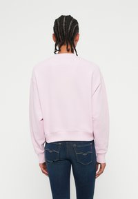 Ανοιχτό ροζ κοντό φούτερ με χαλαρή εφαρμογή και κωνικό μανίκι, σε συνδυασμό με σκούρα τζιν παντελόνια που διαθέτουν ραφή καμπύλης στην πίσω τσέπη.