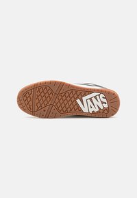 Semelle d'une basket Vans montrant une bande de roulement en caoutchouc marron avec des motifs en losanges et en lignes et un logo Vans blanc au niveau du talon.