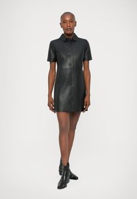 Czarna skórzana sukienka krótka z kołnierzykiem, z przodu na guziki i krótkimi rękawami. Gładka tekstura, dopasowany krój i długość do kolan.