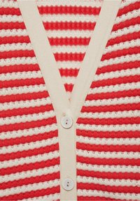 Cardigan rayé rouge et blanc avec un tricot texturé, présentant un décolleté en V, des bordures crème et deux boutons blancs à l'avant.