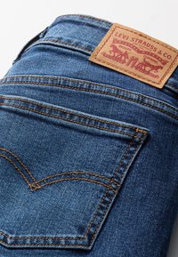 Jean en denim bleu avec une étiquette en cuir marron sur laquelle est embossé "Levi Strauss & Co." Remarquez le détail des coutures de la poche arrière caractéristiques.