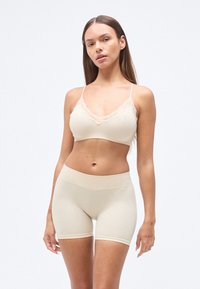 Brassière beige sans coutures avec bordure en dentelle et bretelles réglables, associée à un shorty beige taille haute, texture lisse, design ajusté.