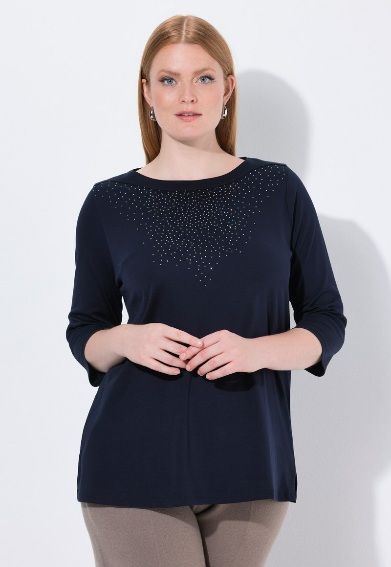 Camicetta blu navy con colletto tondo, maniche a 3/4, presenta un gradiente di piccole pietre luccicanti sul petto, tessuto morbido e spacchi laterali.