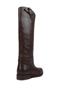 Bota castanha de couro até ao joelho com uma textura suave, bico redondo e um detalhe decorativo de fivela na lateral, perto do topo. Sola plana.