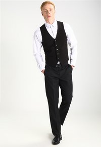 Schwarzer Weste über einem weißen Hemd mit Knöpfen, kombiniert mit schwarzen Anzughosen und -schuhen. Sie hat einen schlanken Schnitt mit fünf Knöpfen und einem eleganten Design.