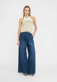 Top halter in maglia leggera con righe orizzontali, abbinato a pantaloni in denim blu a gamba larga. Dettaglio notevole: tessuto testurizzato e vestibilità morbida.