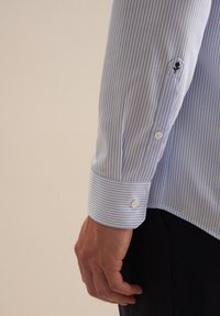 Camicia a righe blu chiaro e bianca con polsini abbottonati, caratterizzata da un piccolo dettaglio ricamato sulla manica sinistra.