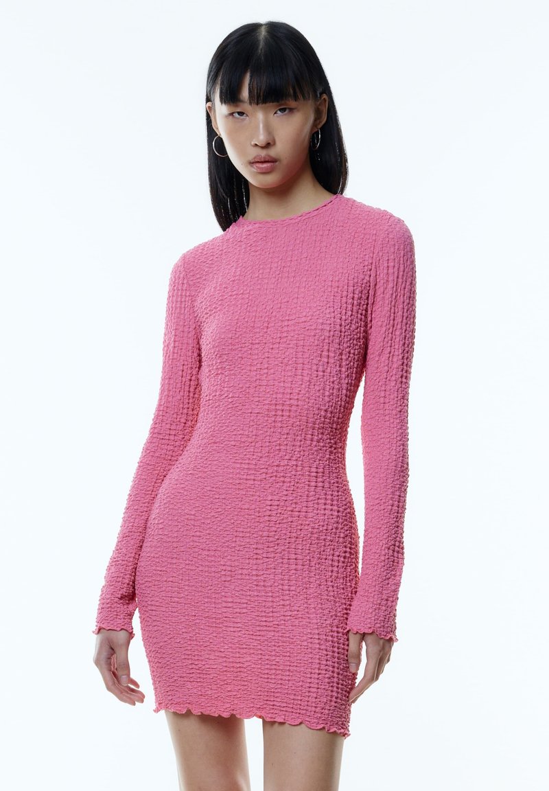Kurzes rosa Kleid aus strukturiertem Stoff, mit langen Ärmeln und einem wellenförmigen Saum, eng anliegendem Schnitt und rundem Ausschnitt.