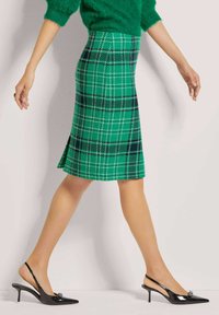 Groene geruite rok van een wolmix stof, met witte en donkerblauwe lijnen, onder de knie met een lichte flare en een split aan de achterkant.