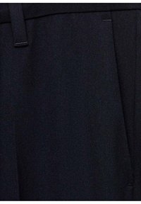 Gros plan d'une poche de pantalon en tissu noir avec passant de ceinture visible et détails de la couture latérale.