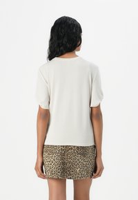 Short-sleeve, cream-colored top with a round neckline. Paired with a leopard-print mini skirt, showcasing a smooth texture and fitted design.