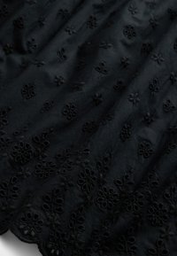 Tessuto nero con ricamo floreale e dettagli ritagliati. Superficie strutturata con una leggera lucentezza, caduta fluida e orlo smerlato.