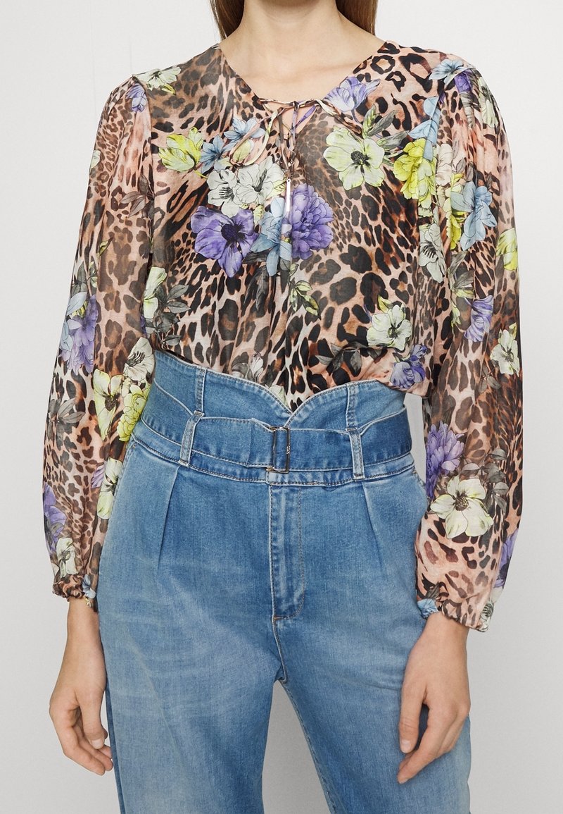 Blouse à manches longues avec imprimé floral et léopard, col à nouer, associée à un jean en denim bleu taille haute plissé avec boucle de ceinture.