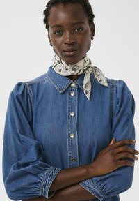 Blusa in denim con scollo a collo, chiusura frontale con bottoni, maniche a sbuffo e vestibilità larga. Abbinala a una sciarpa bianca e nera con motivo.