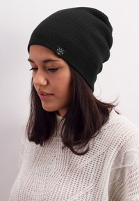 Black ribbed knit beanie with a slouchy fit, featuring a small black and white logo tag on the side.
