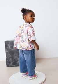 T-shirt graphique colorée à manches courtes, ornée de motifs floraux et de dessins animés ; associée à un jean en denim bleu ample et des baskets multicolores.